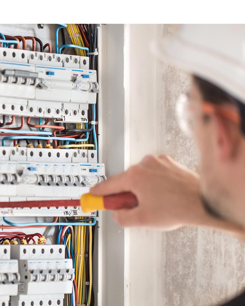 Man, an electrical technician working in a switchboard with fuses. Installation and connection of electrical equipment. Professional with tools in hand. concept of complex work, space for text.